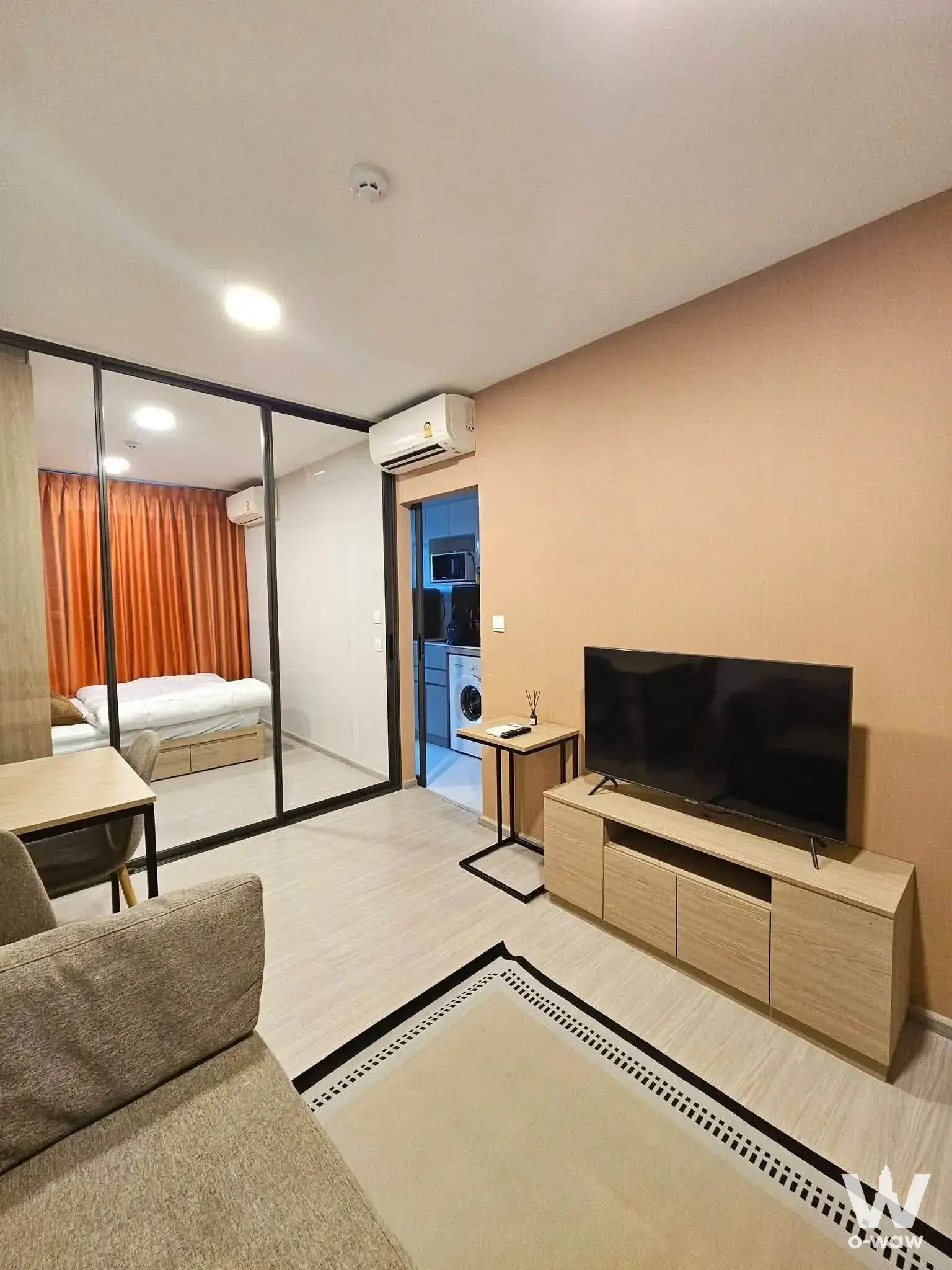 Open-plan 1-bed condo for rent in The Privacy S101 featuring a glass partition, peach accent wall, and minimalist furnishings