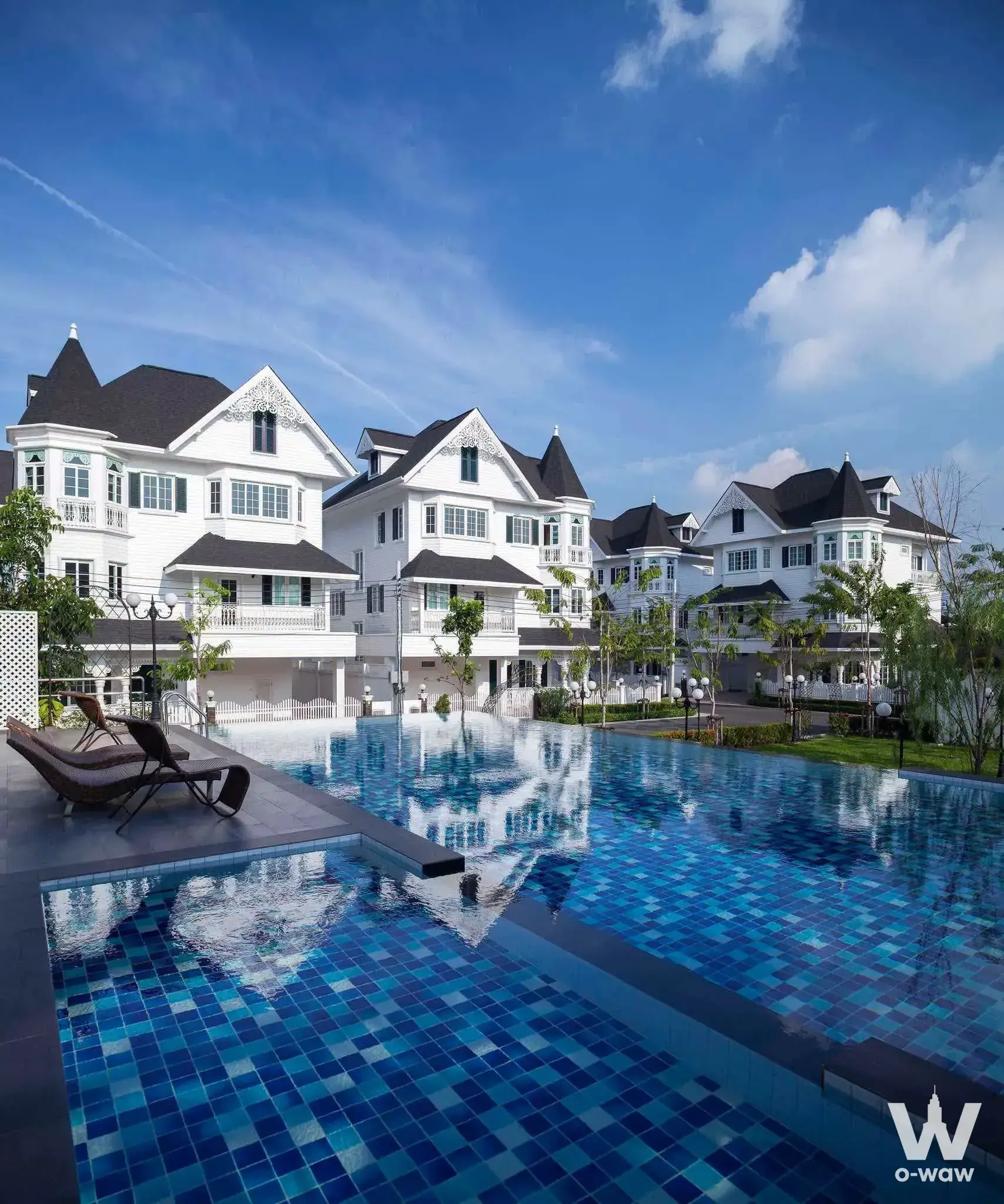 Fantasia Villa Bangna poolside view with wicker loungers and white townhouses featuring black gabled roofs