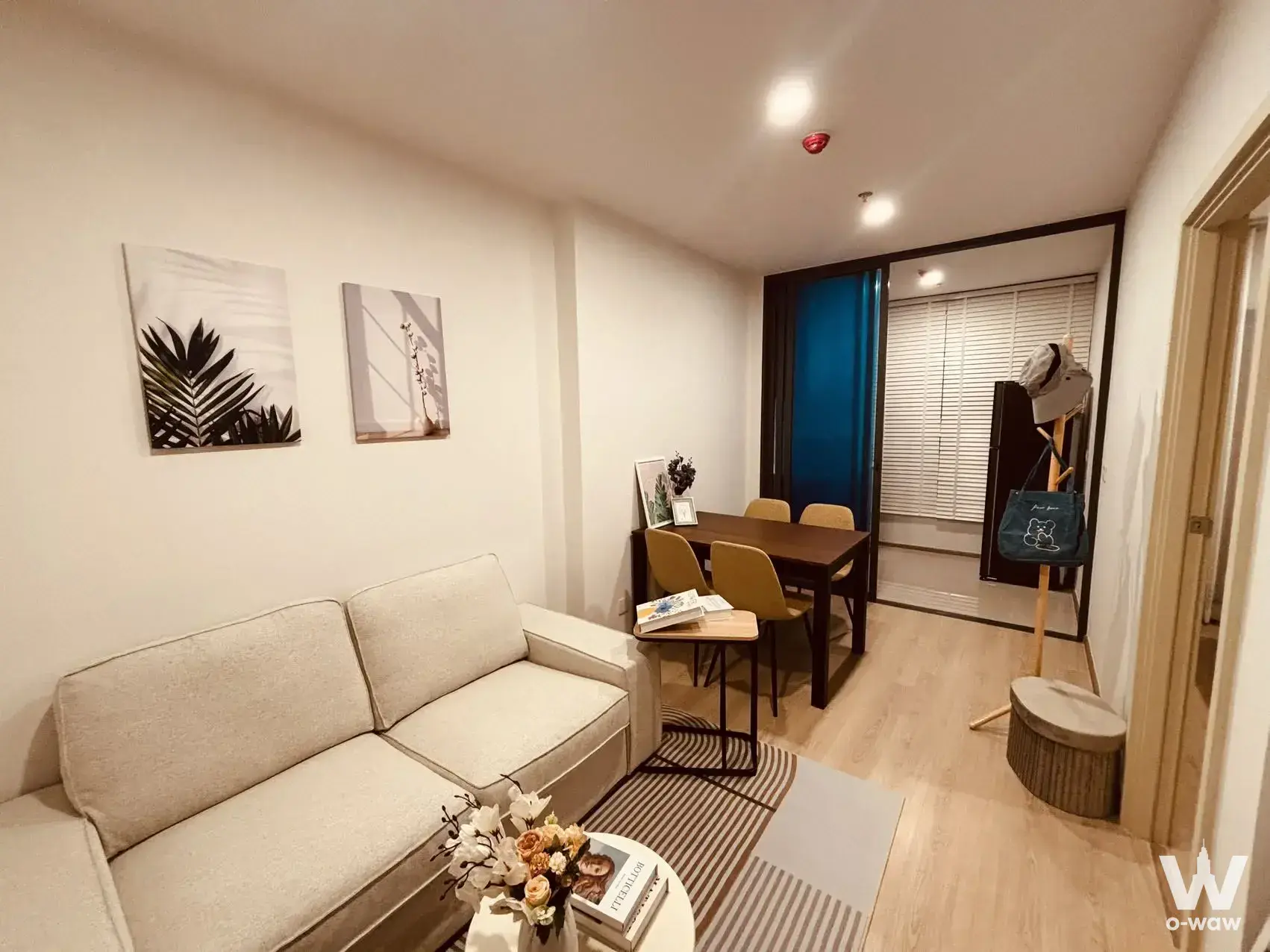 Modern condo living-dining area with beige sofa, mustard chairs, light wood floors, and sliding glass door to balcony