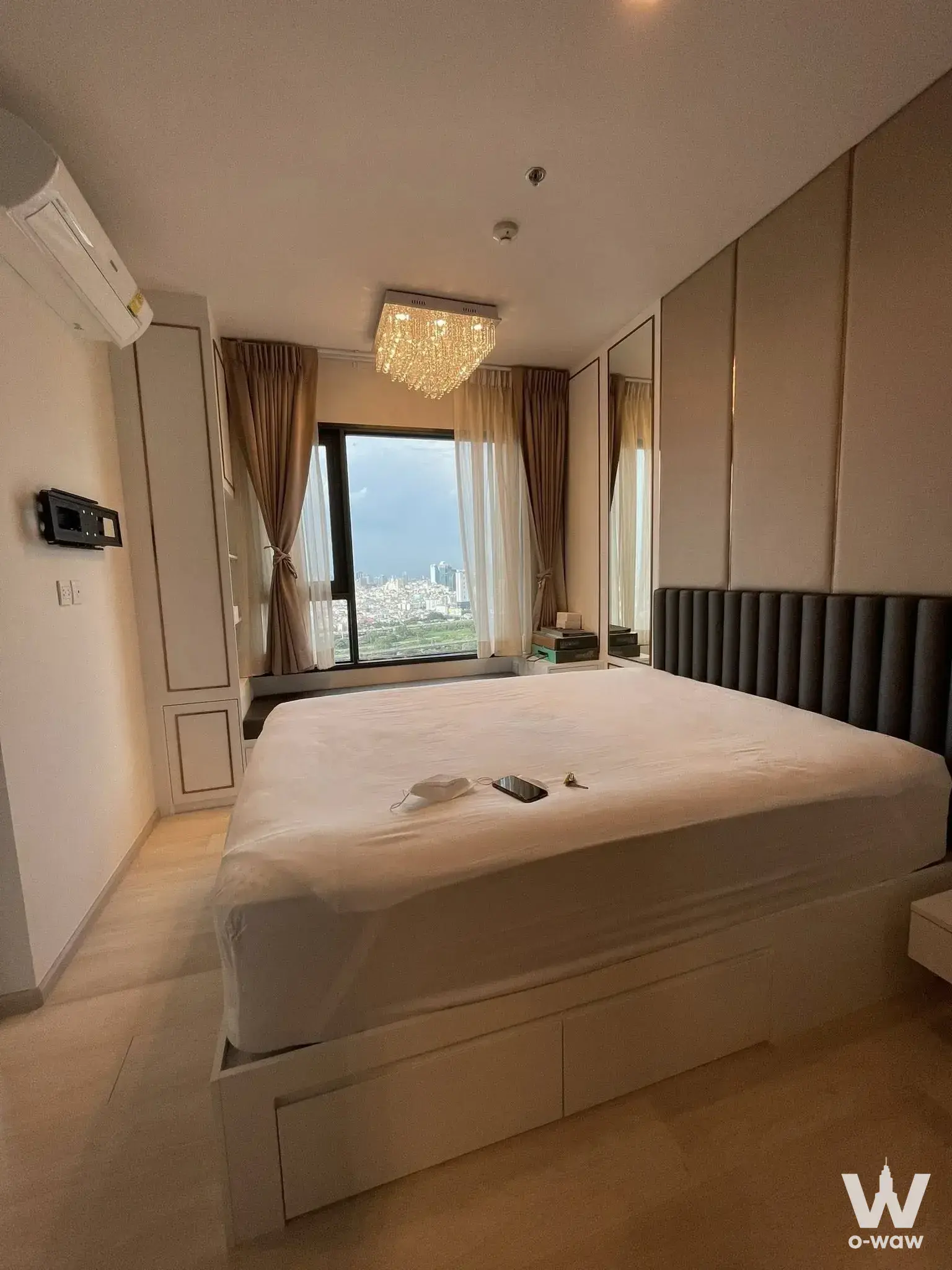 Life One Wireless bedroom with crystal chandelier, king-size bed, and city skyline view through large window