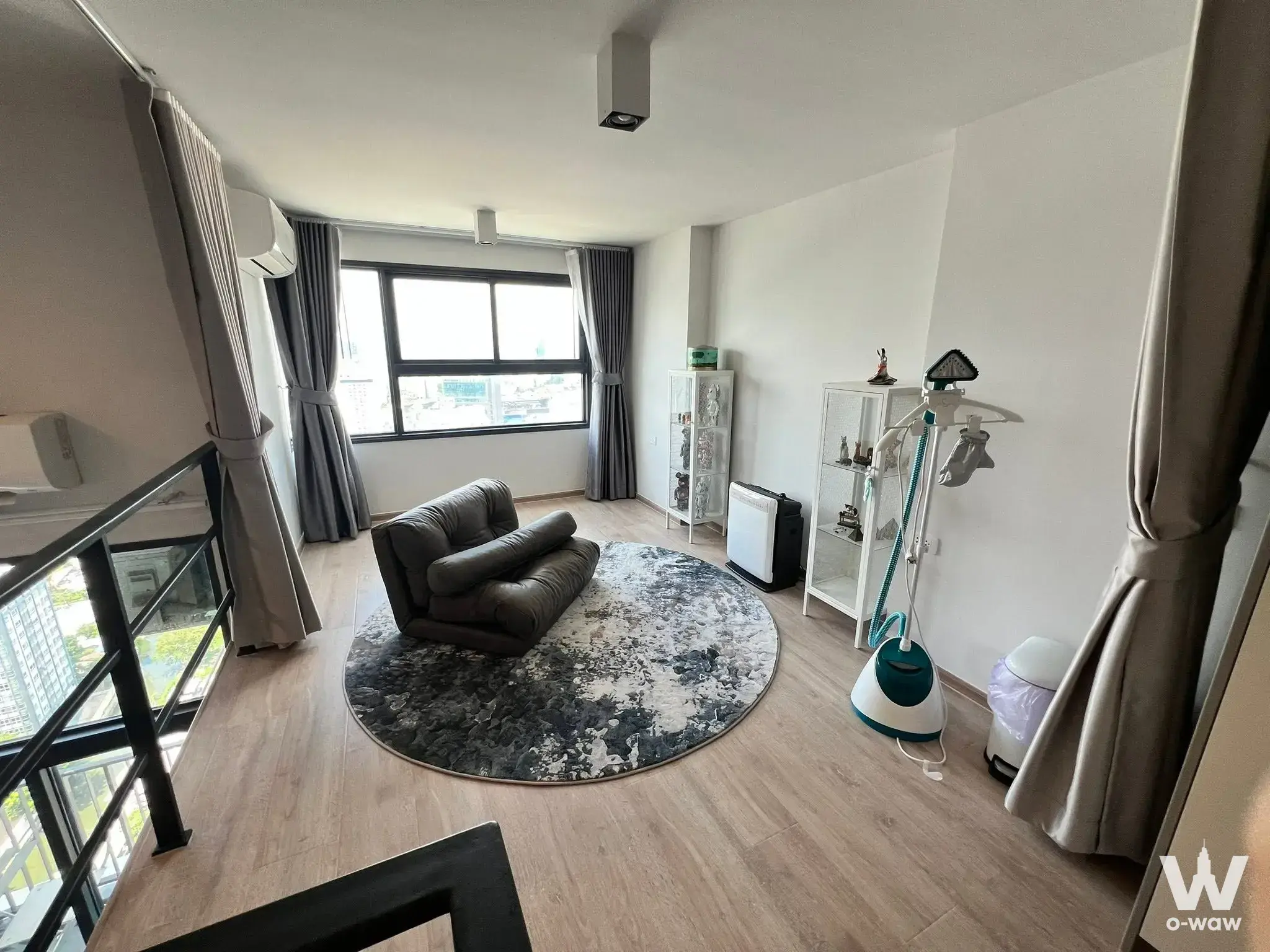 Modern loft living area in IDEO Rama 9 condo with grey sofa, light wood floors, and glass railing overlooking lower level
