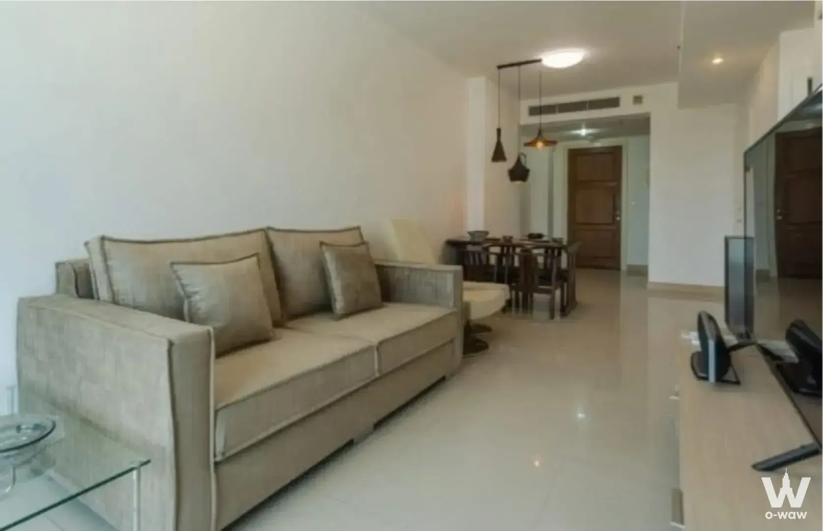 Modern living room in Supalai Casa Riva Vista 1 condo with beige sofa, glass coffee table, and dark wood dining set under