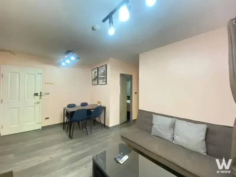 This open-plan 2-bed condo living area in My Condo Sukhumvit 81 has a grey sofa, dining table and blue chairs
