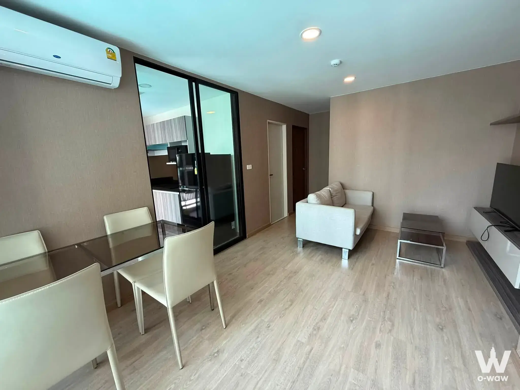 Modern living dining area with glass table white sofa and kitchenette view in 2-bed condo for sale at The Cube Urban Sathon