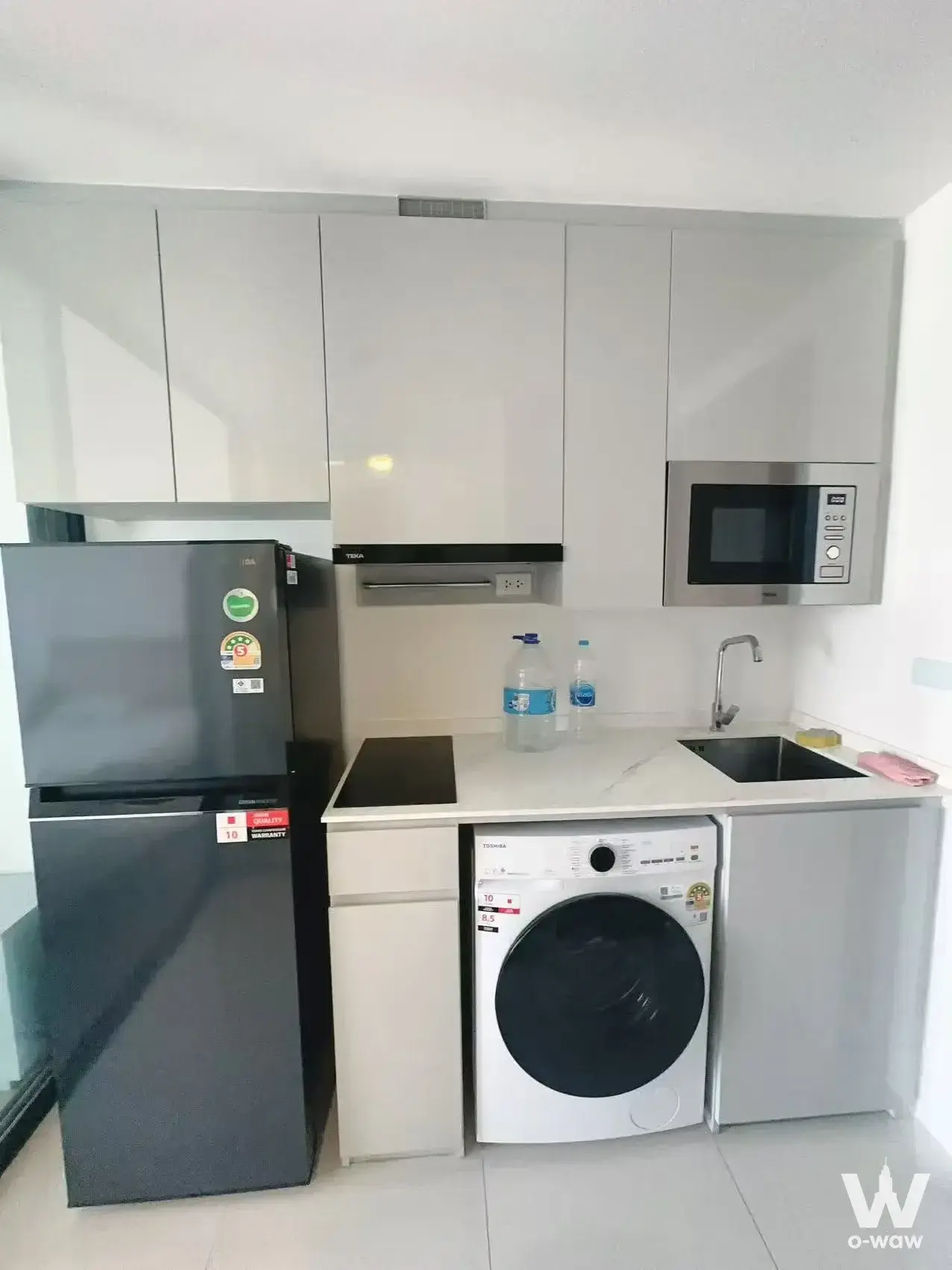 Compact kitchenette in SOHO Bangkok Ratchada 1-bed featuring white cabinets and built-in appliances