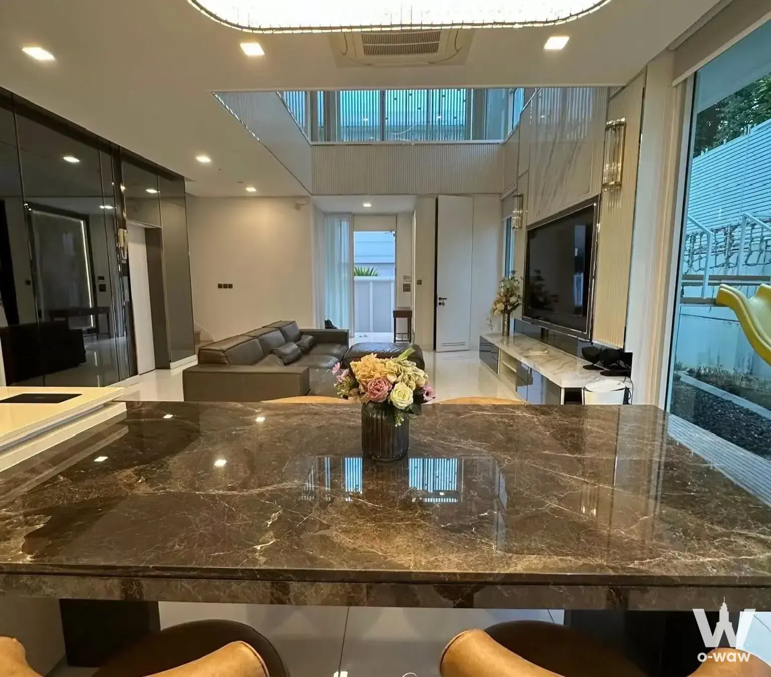 Modern open-plan living and dining area with high ceilings, marble kitchen island, grey sectional sofa, and glass doors to