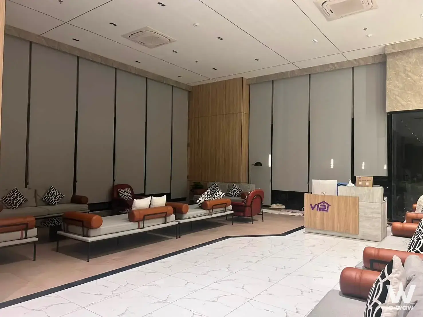 Condo lobby reception with light wood desk, grey sofas, and red leather accent chairs