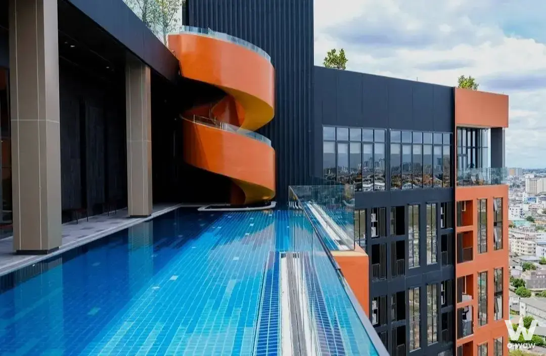 The FLO by Sansiri rooftop pool deck shows an infinity pool and orange spiral staircase