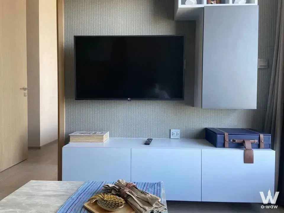 Modern living room in THE ESSE ASOKE 1-bed condo with wall-mounted TV, white media console, and marble coffee table