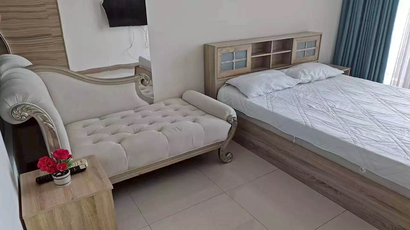 Bright bedroom in 1-bed Riviera Jomtien rental with wooden bed, chaise lounge, and teal curtains