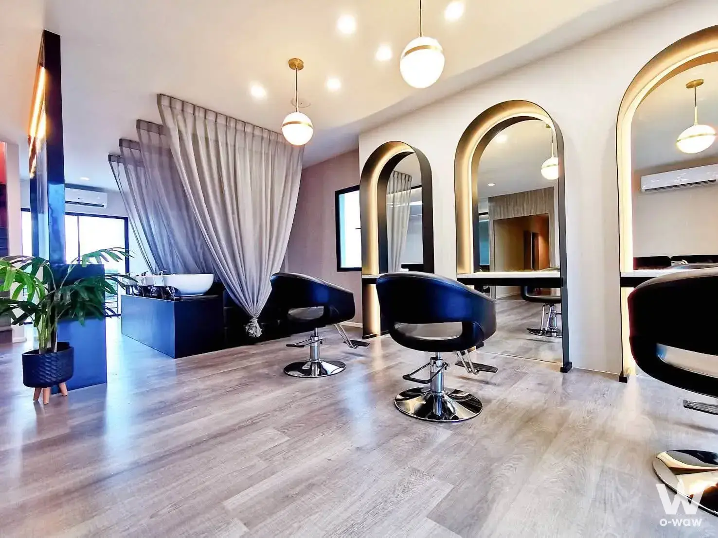 Modern salon interior with black styling chairs, gold-trimmed arched mirrors, and blue washing station in Cascade Bangna