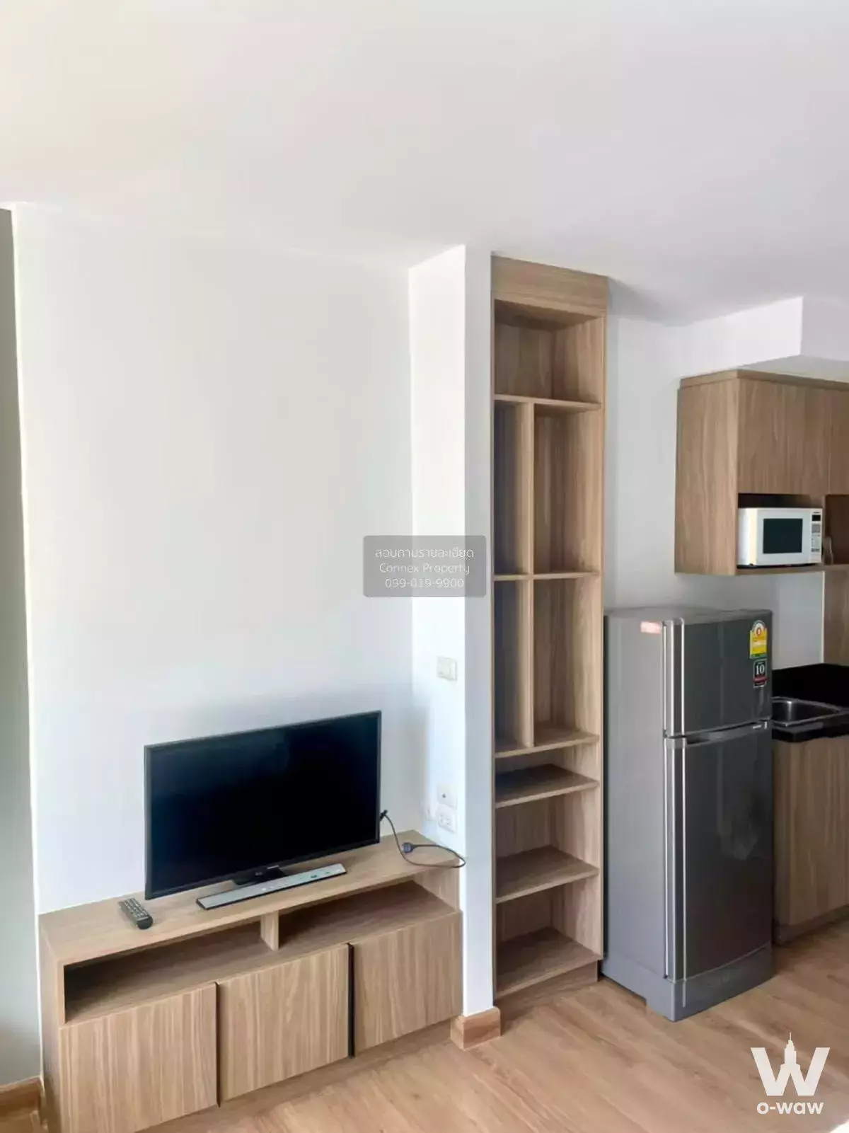 Modern 1-bed condo living area at Chapter One Ladprao with light wood flooring, TV console, and compact kitchenette
