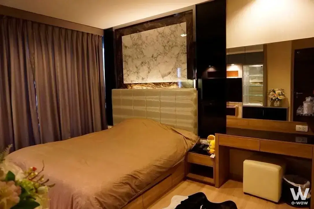 Modern bedroom with beige upholstered headboard, white marble accent wall, and wooden vanity desk