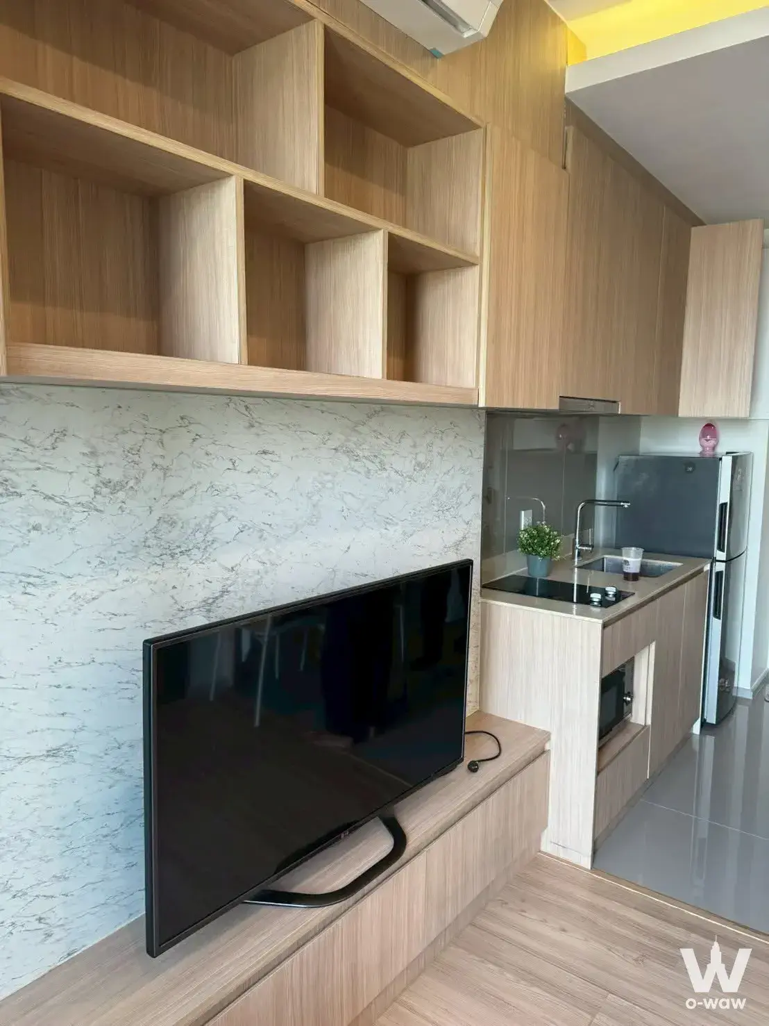 Modern 1-bed condo living area in M Jatujak with light wood floors, open shelving, and compact kitchenette