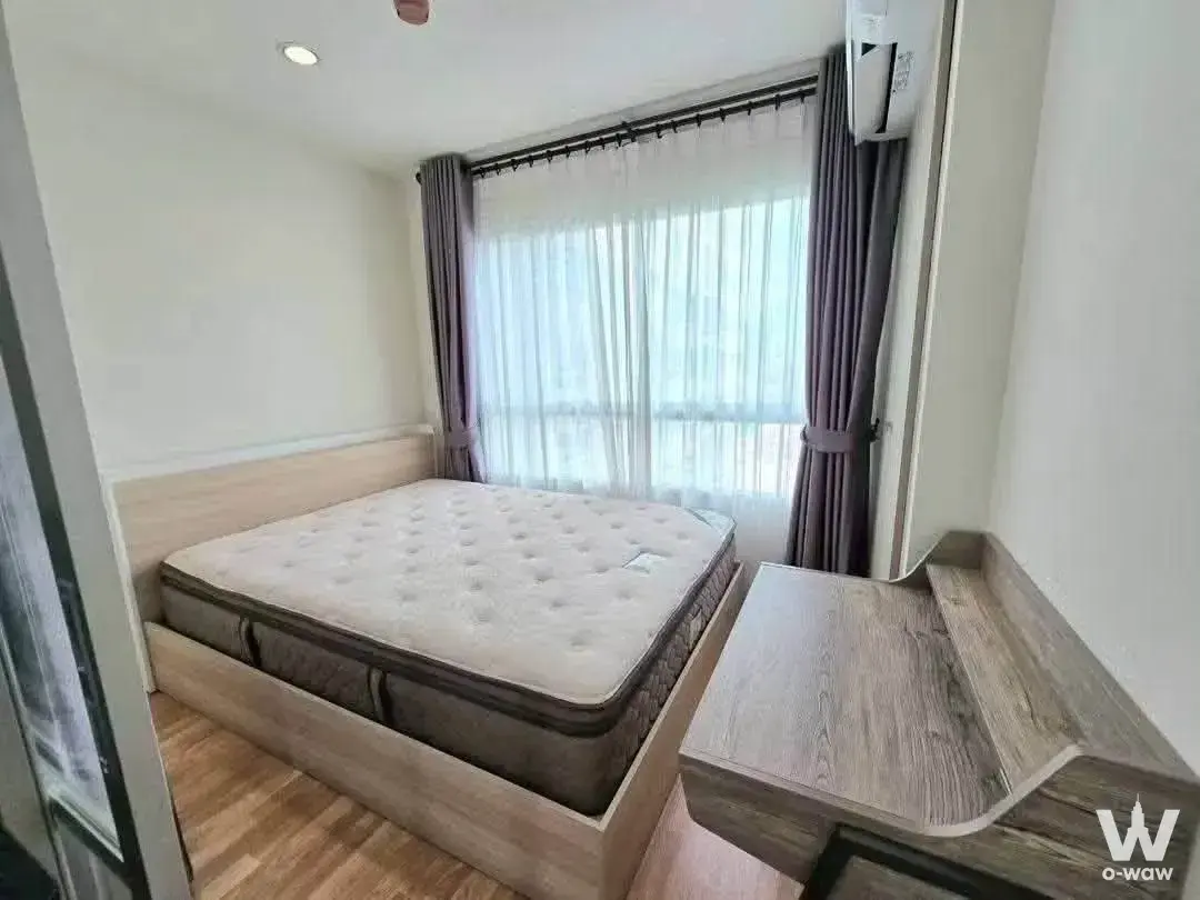 Minimalist bedroom with light wood bed and desk in a 1-bed condo for sale at Lumpini Ville Nakhon In Riverview