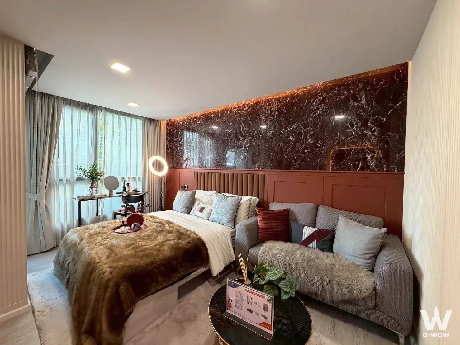 Queen bed and sofa in 1-bed condo for sale at Atmoz Tropicana Bangna with wood paneling and cove lighting