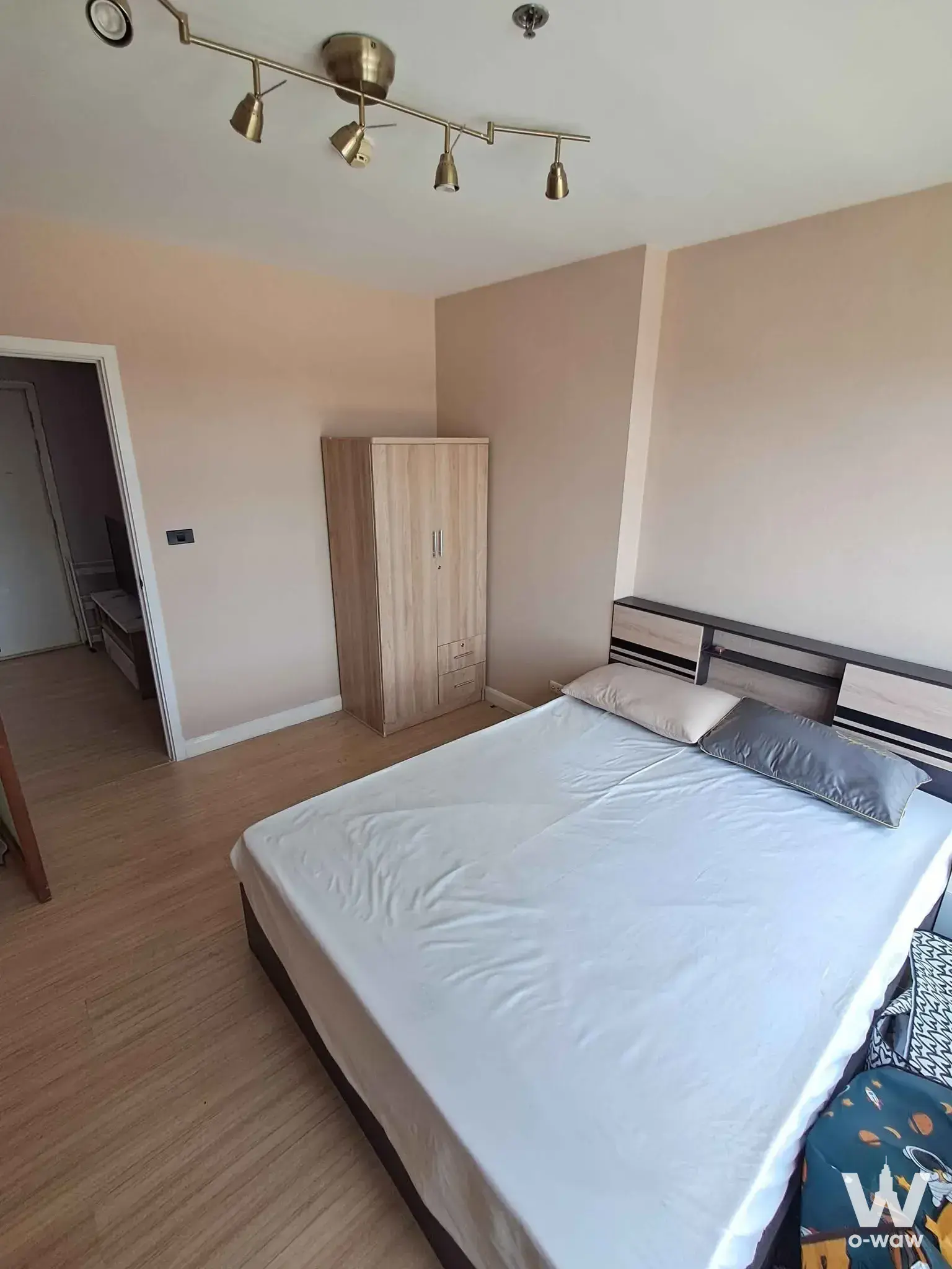 Modern bedroom with queen bed, light wood wardrobe, and brass track lighting in 1-bed rental at Fuse Sense Bangkae