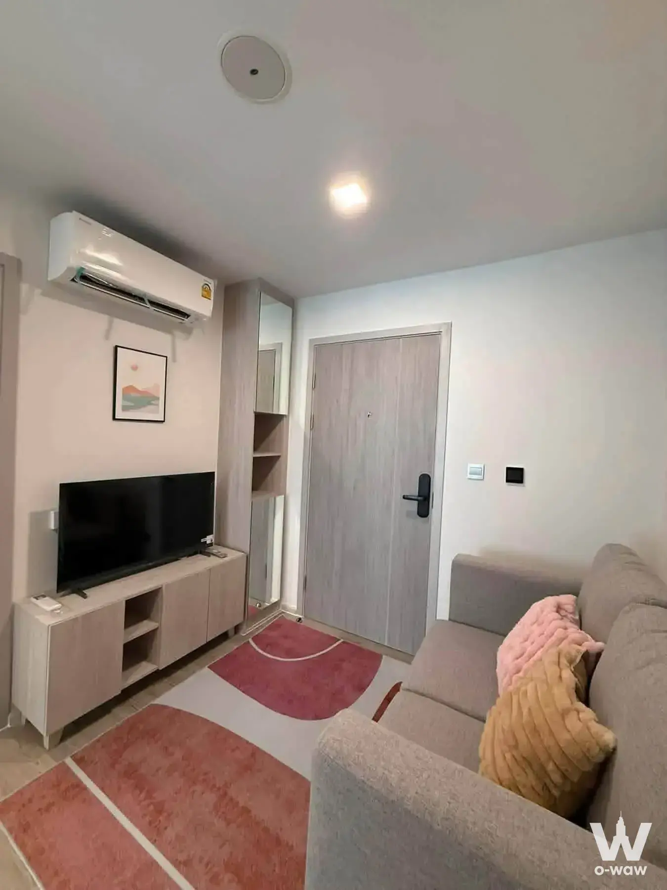 Light-grey sofa with pink accents and wood-grain storage in a furnished 1-bed condo for rent at KAVE Seed Kaset