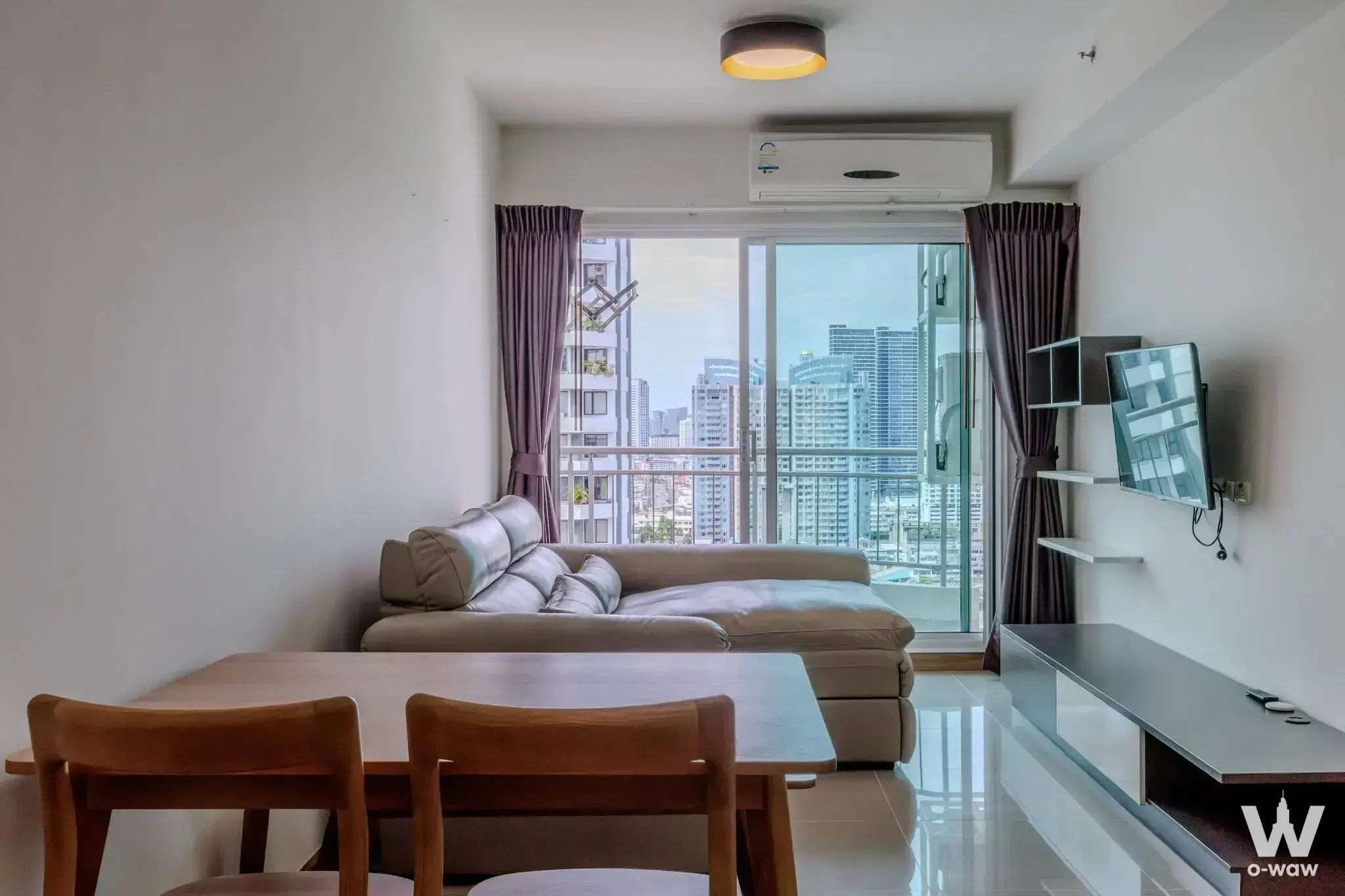 Living room in Supalai River Resort with beige leather sofa and city skyline view through sliding doors