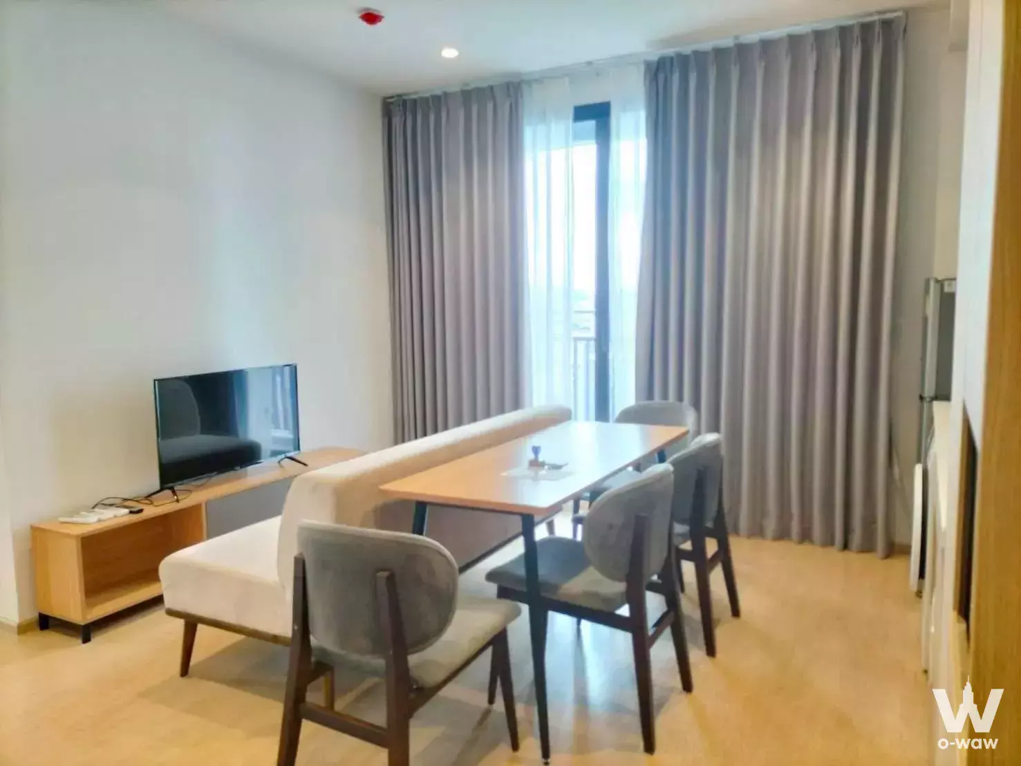 Modern living and dining area with light wood floors, sofa, and balcony access in 2-bed condo for rent at M Ladprao