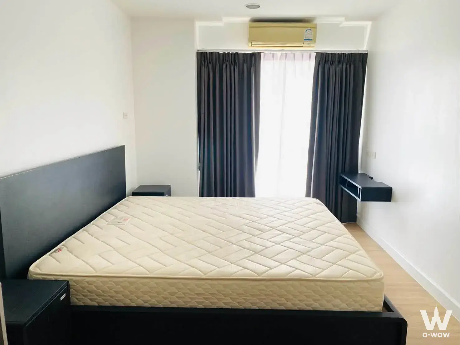 Punnawithi 1-bed condo bedroom featuring a dark wood platform bed and minimalist layout