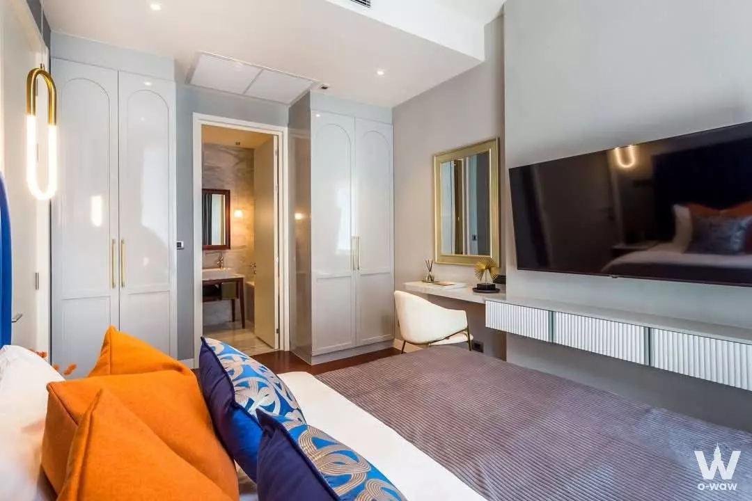 Modern bedroom in KHUN by YOO 1-bed rental with queen bed, orange accents, dark wood floors and en-suite bathroom view