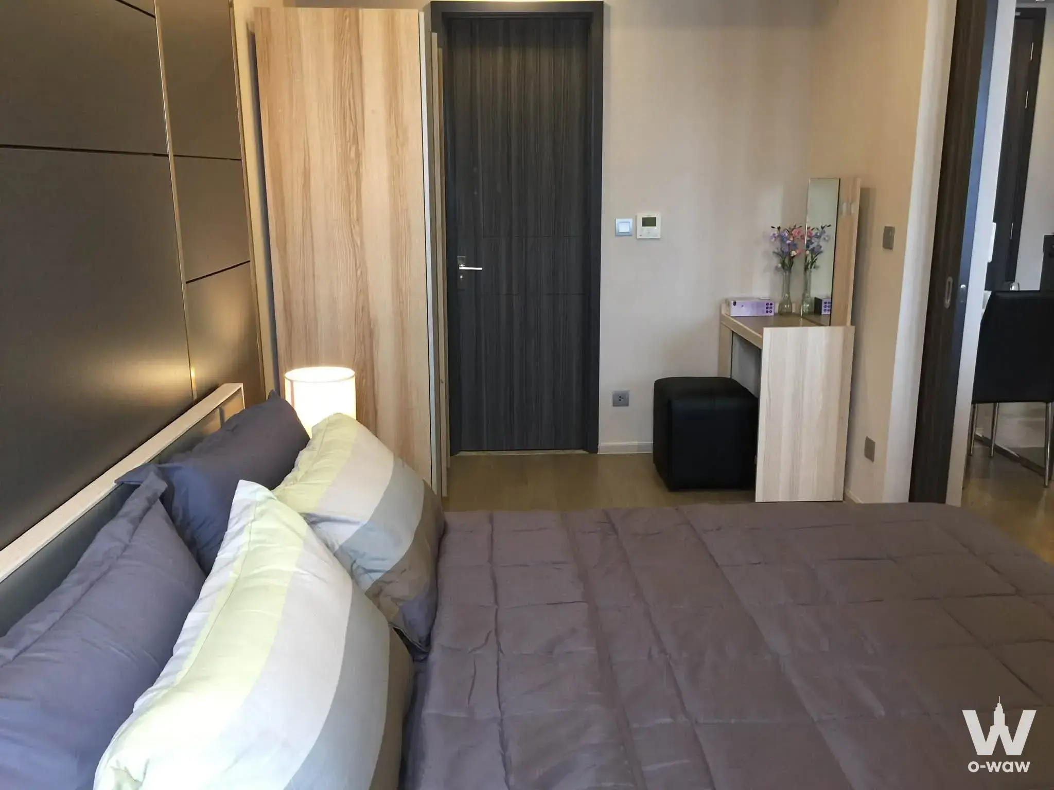 Grey queen bed beside dark wardrobe and vanity desk in a modern 1-bed condo for rent at Ashton Asoke