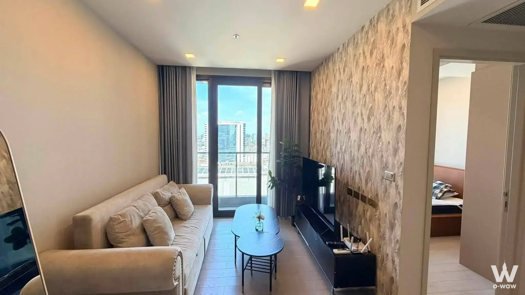 Spacious living room in a One9Five Asoke condo with beige sofa, marble tables, and high-floor city skyline views
