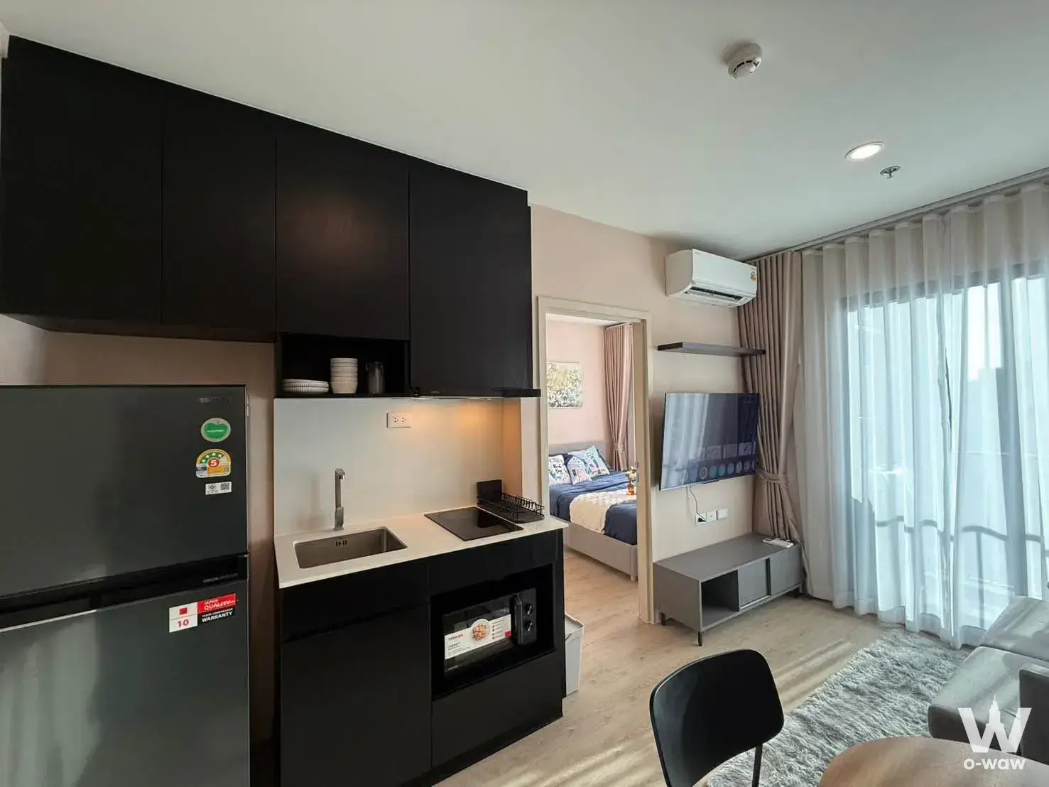 Modern studio with glossy black kitchen cabinets and a grey sofa near floor-to-ceiling windows