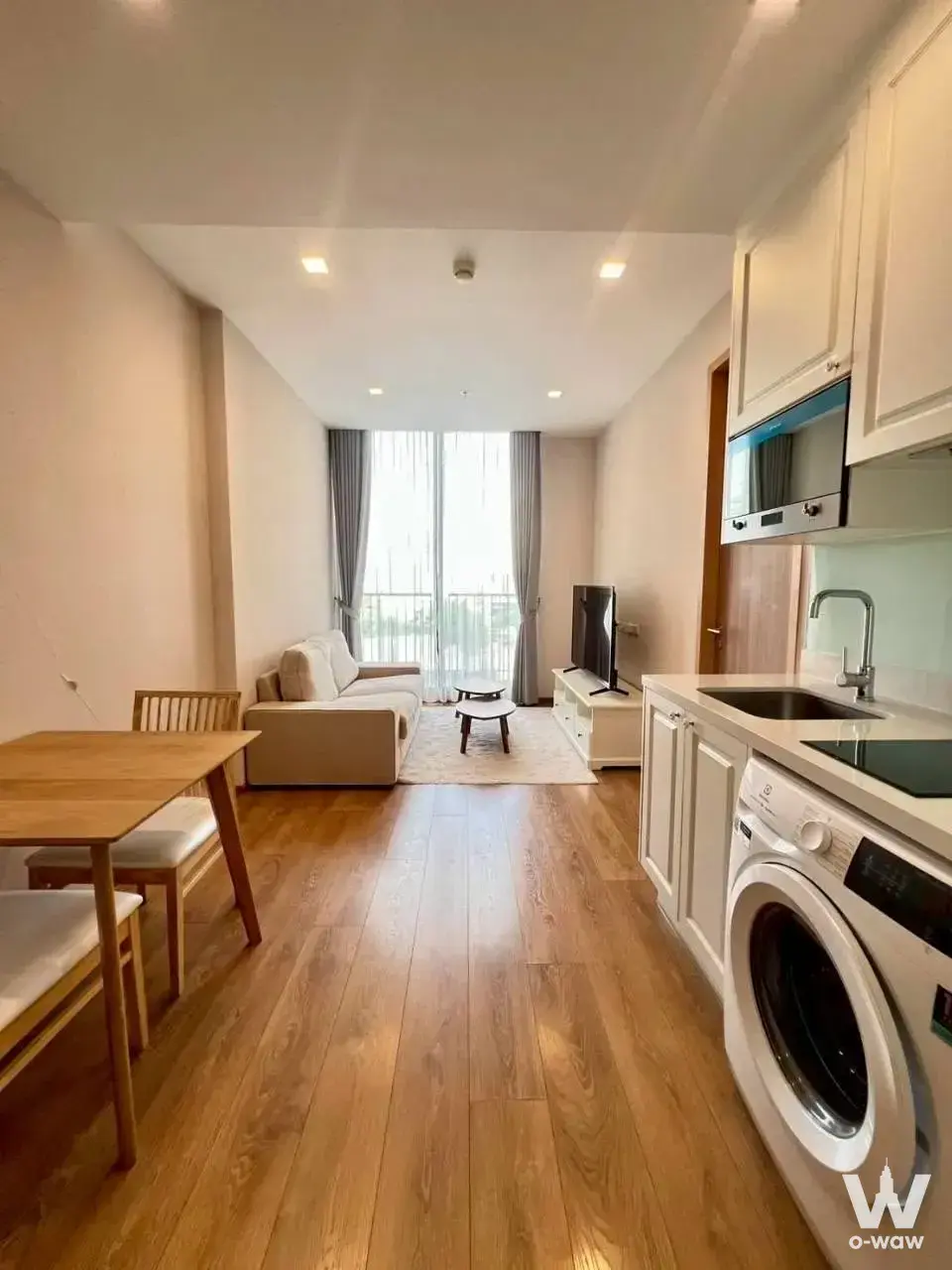 Open-plan living area in a 1-bed condo for rent at Noble BE33 with a cream sofa, white kitchen cabinets, and balcony access