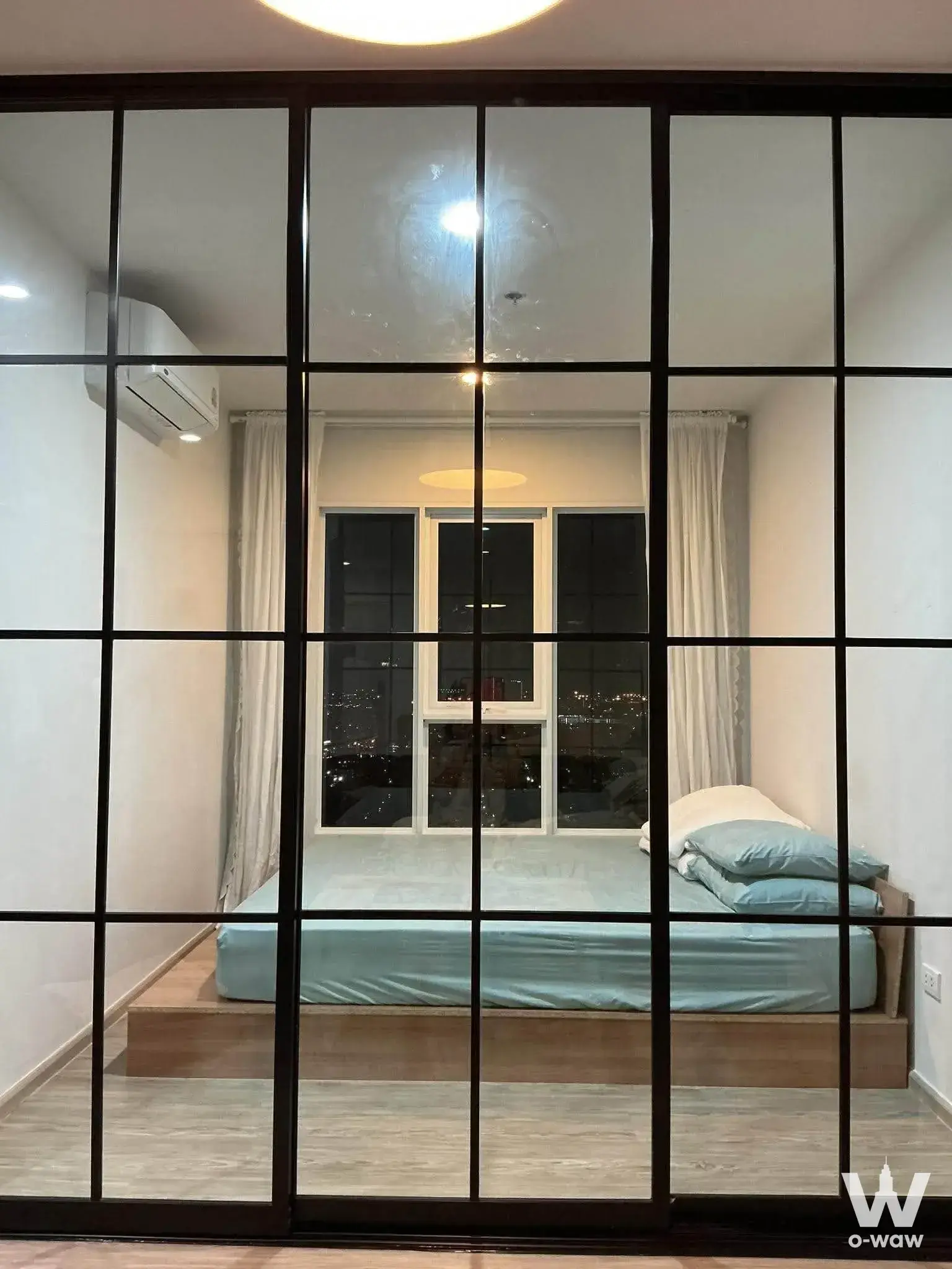 Queen bed with blue bedding in a Regent Home Bangna condo bedroom featuring city views through large windows