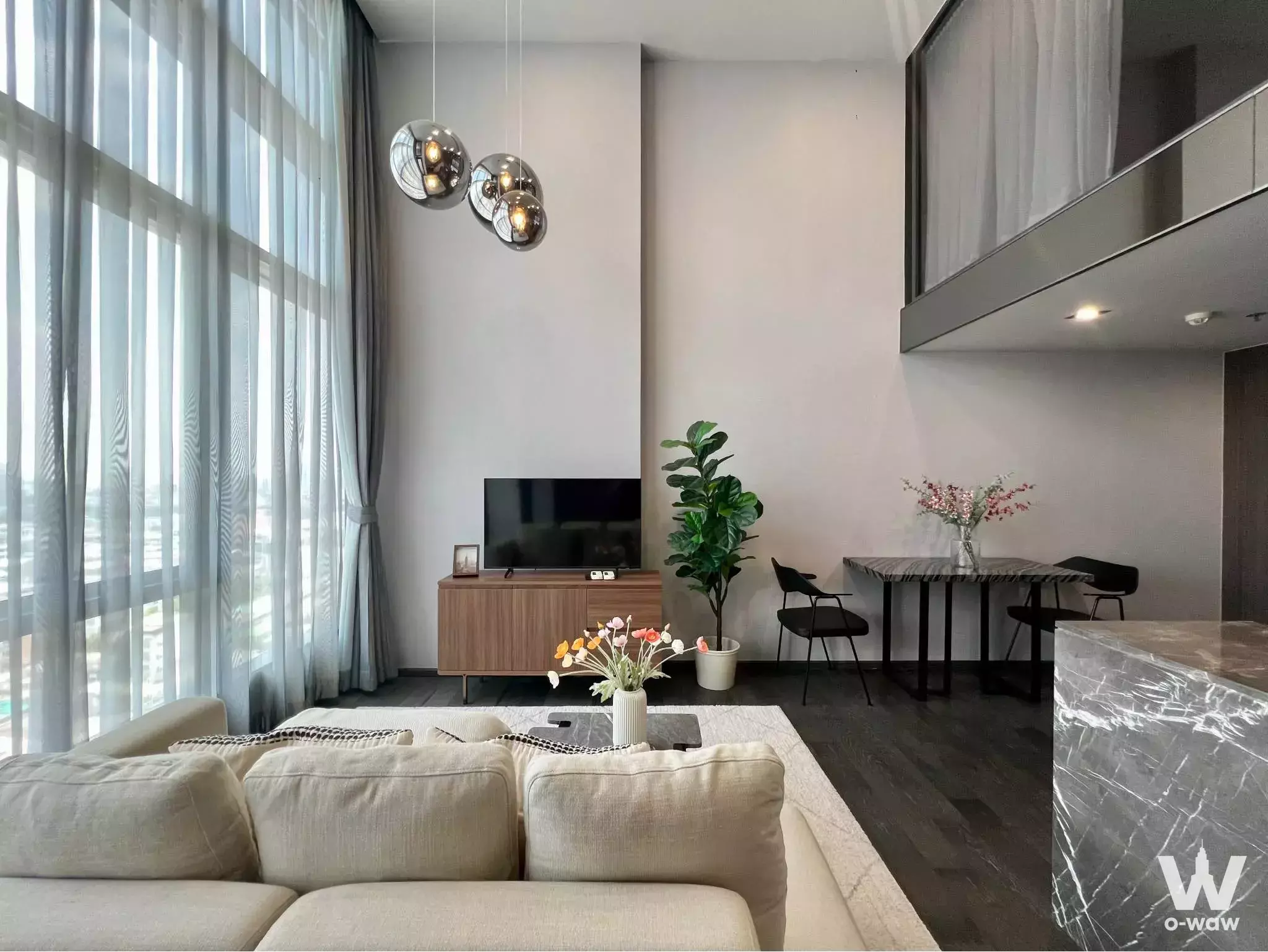 Modern loft living room with beige sofa and mezzanine in 1-bed condo for rent at CONNER Ratchathewi