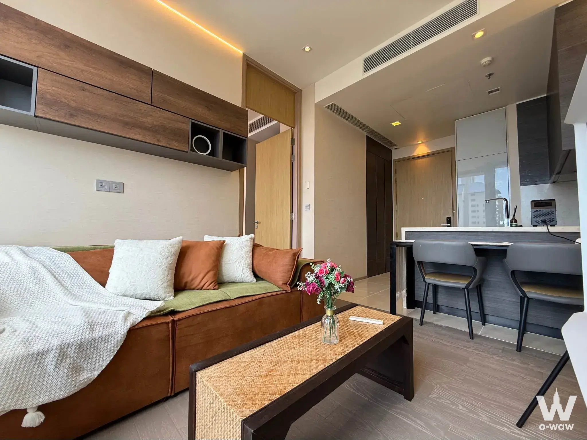 Furnished living area with brown leather sofa and rattan coffee table in 1-bed condo for rent at THE ESSE ASOKE