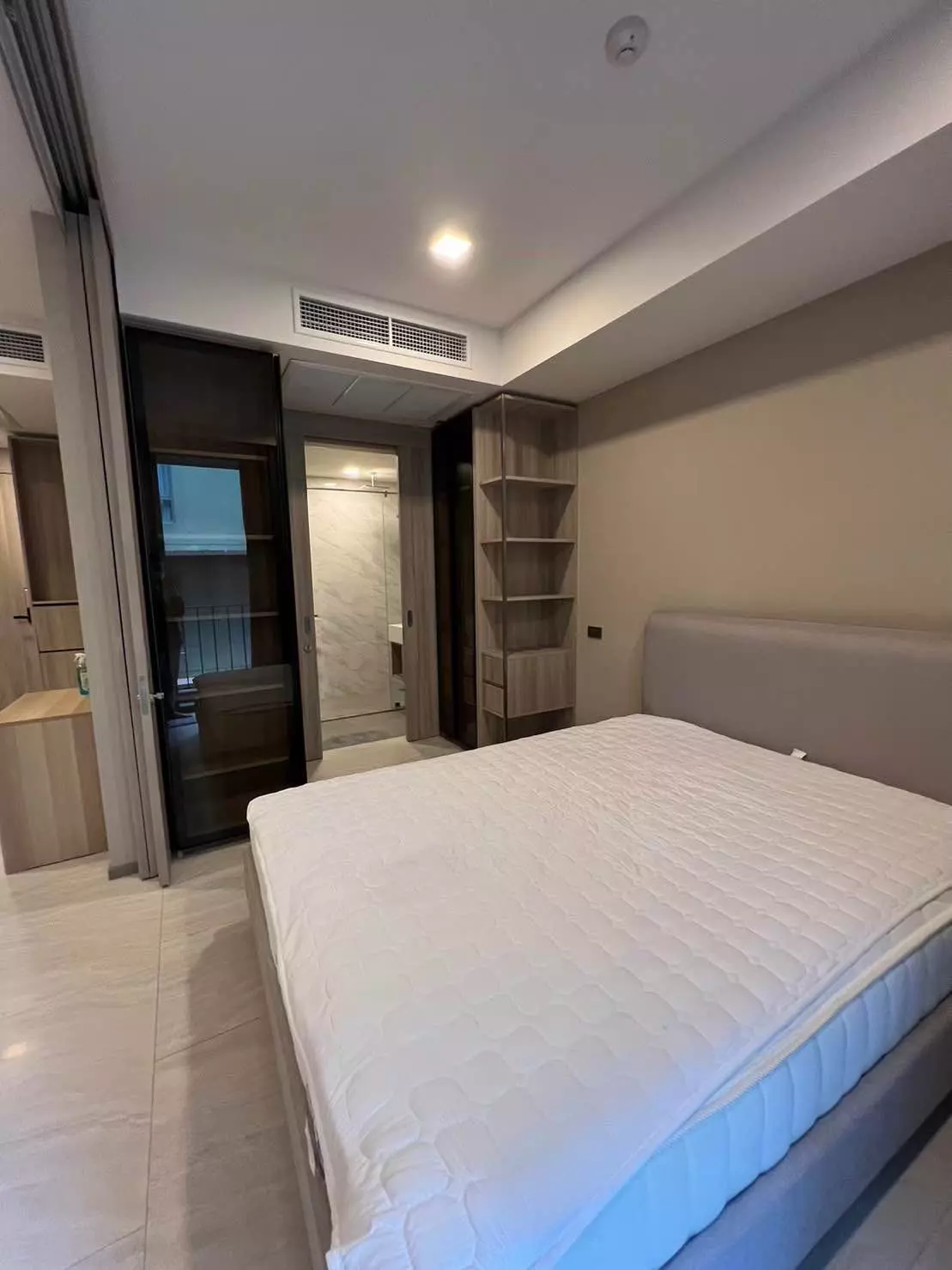 Modern bedroom in 1-bed condo for rent at Fynn Sukhumvit 31 with queen bed, light wood shelving, and glossy cream tiles