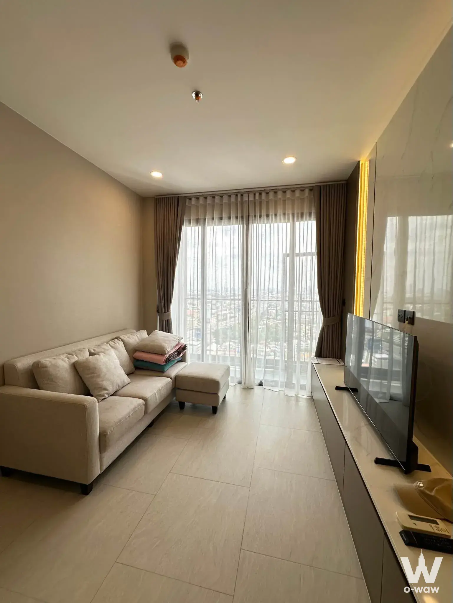 Living room in a 2-bed Cooper Siam condo with beige sofa, LED-lit wall panel, and full-height balcony doors