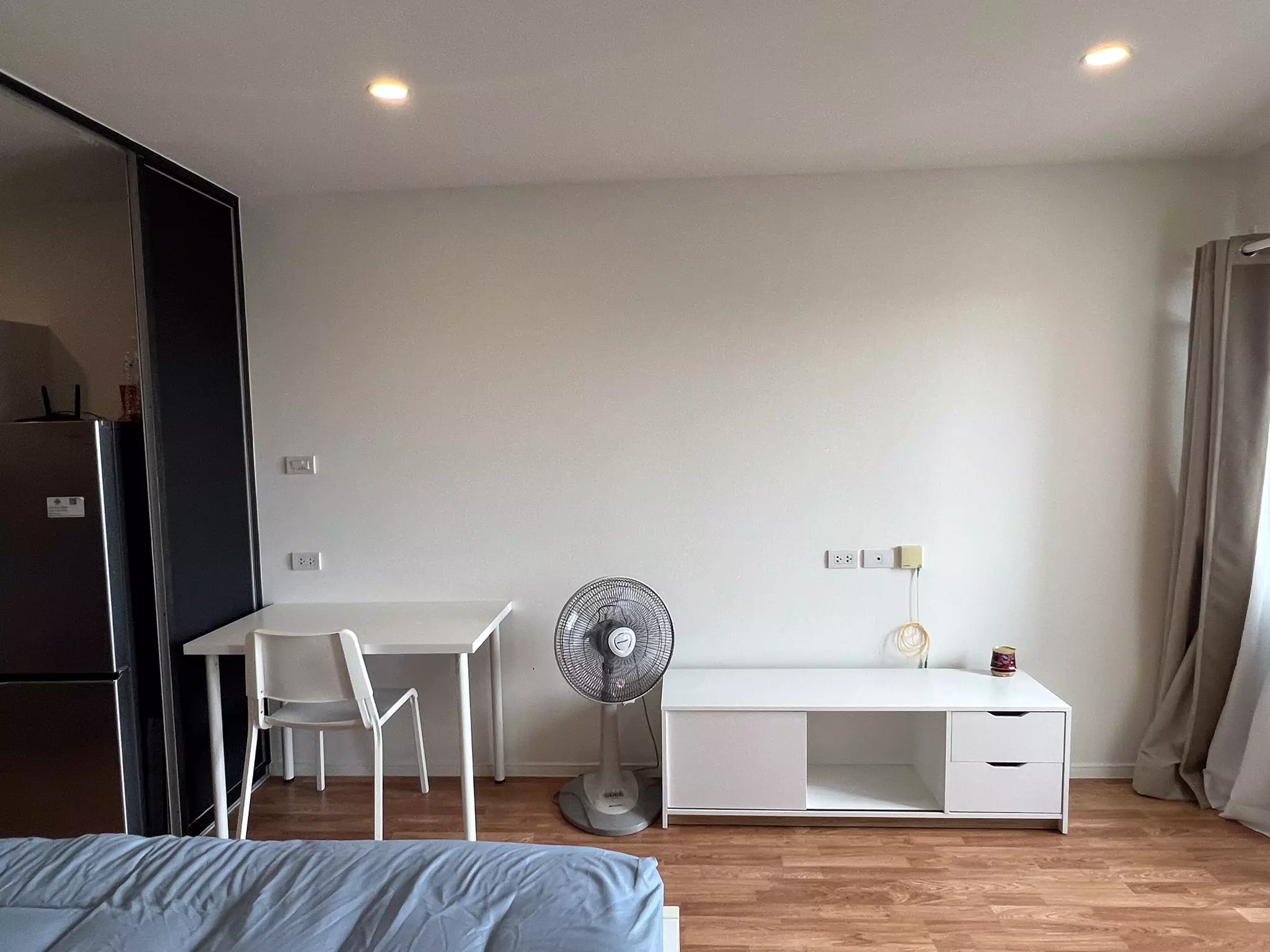 Modern 1-bed condo bedroom in Lumpini Ville Pattanakarn with wood floors, white walls, and beige curtains