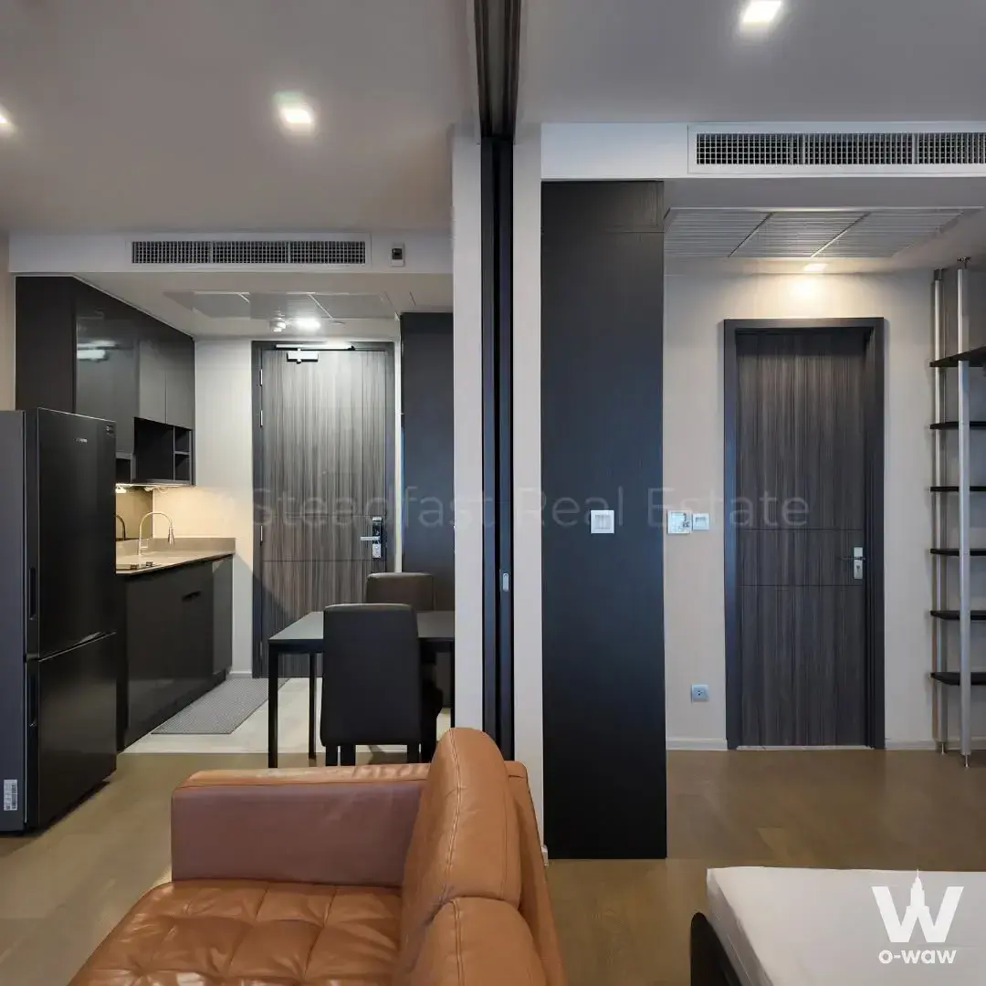 Modern 1-bed condo for rent in Ashton Asoke with tan sofa, dark cabinets, and light wood floors