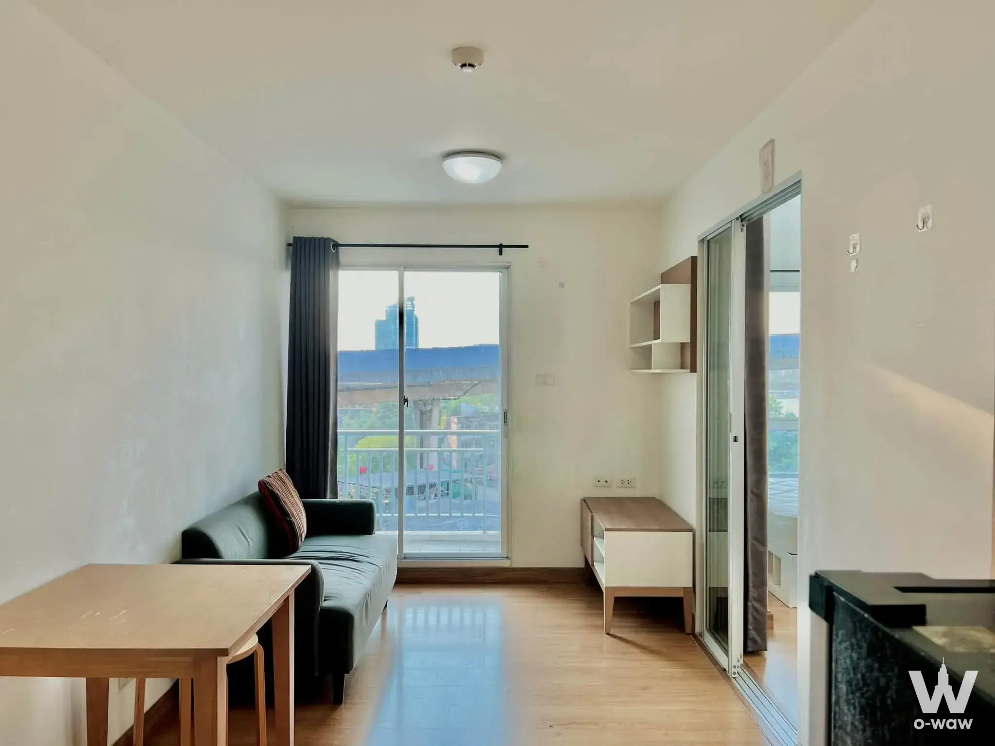 Living room of a 1-bed condo for sale in August Condo Charoen Krung 80 featuring dark sofa and balcony view