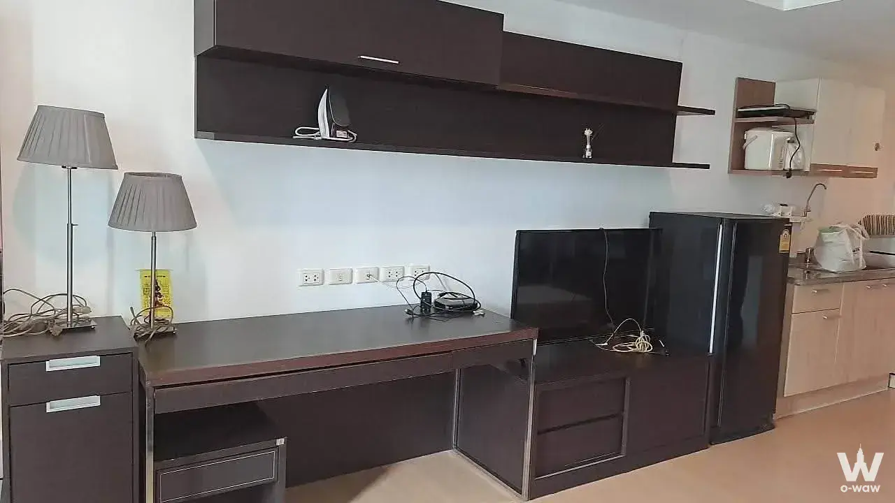 Open-plan studio for rent at The Trendy Condominium with dark wood desk and compact kitchenette