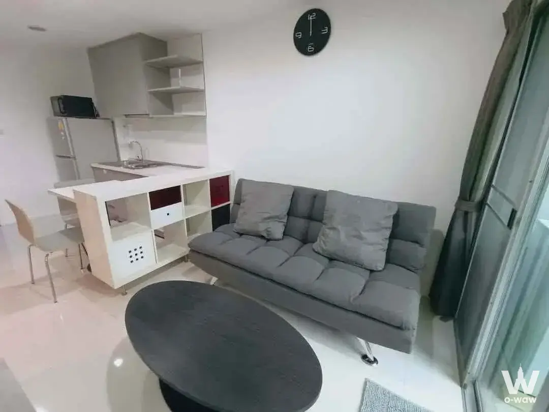 Open-plan studio with grey sofa and compact kitchenette in a 1-bed condo for rent in Punnawithi