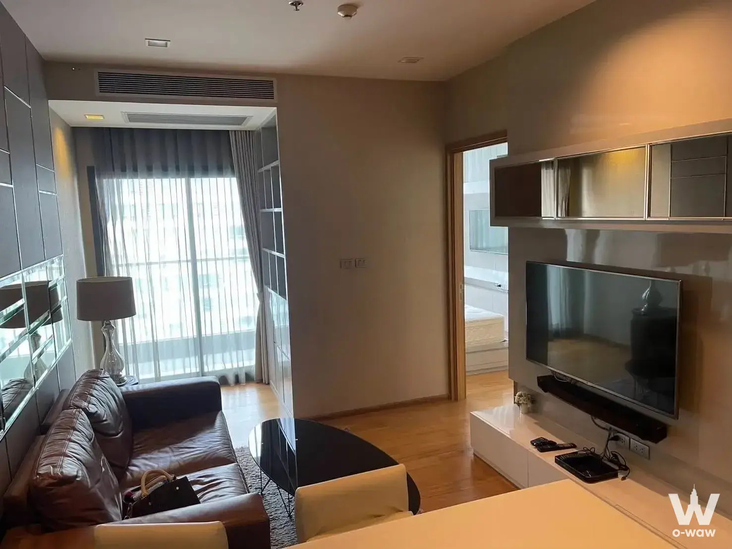 Modern living room in 1-bed Hyde Sukhumvit 13 rental with leather sofa, TV console, and city views
