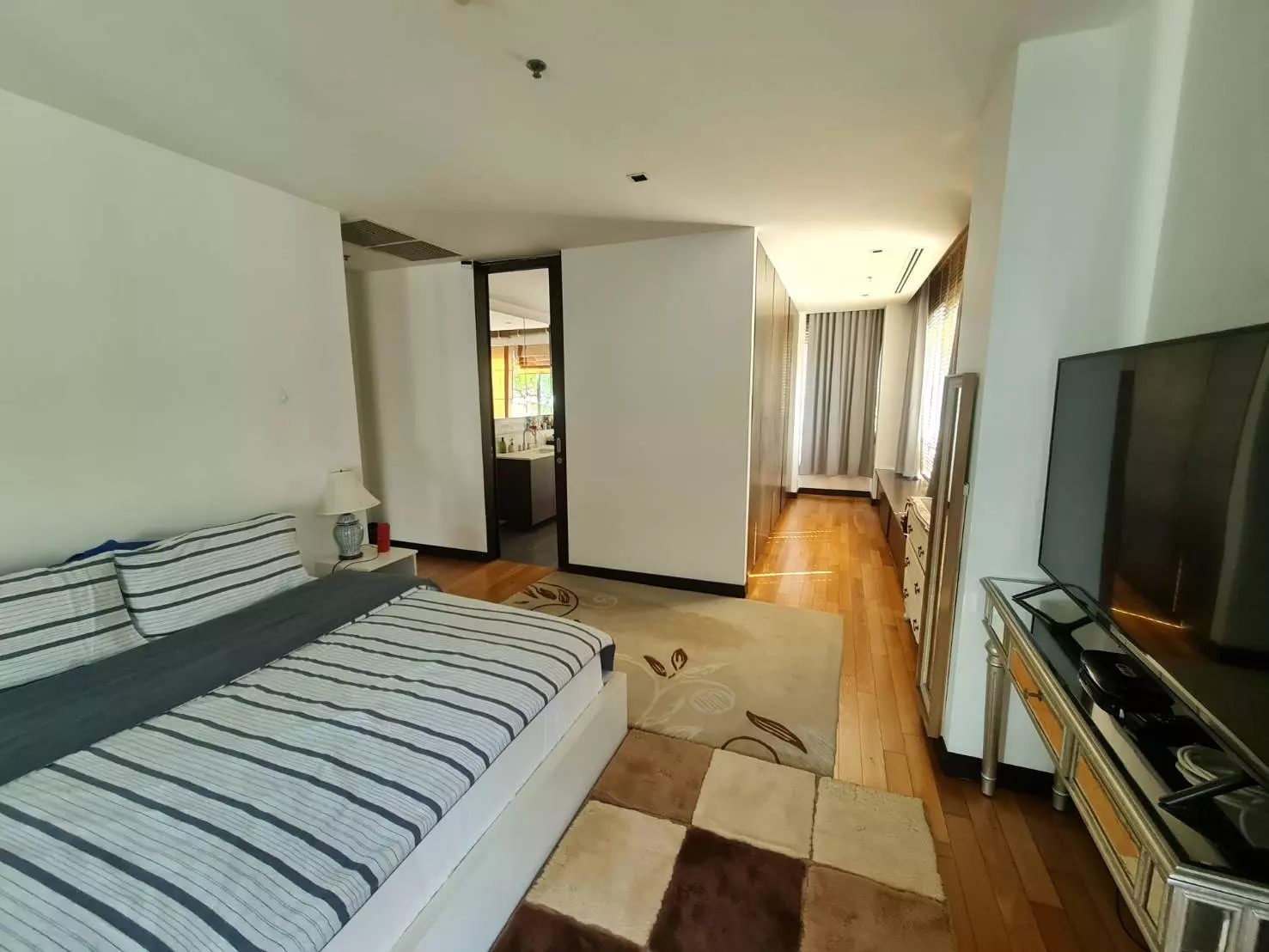 Modern bedroom with hardwood floors, striped linens, mirrored TV console, and en-suite bathroom access in The Lofts
