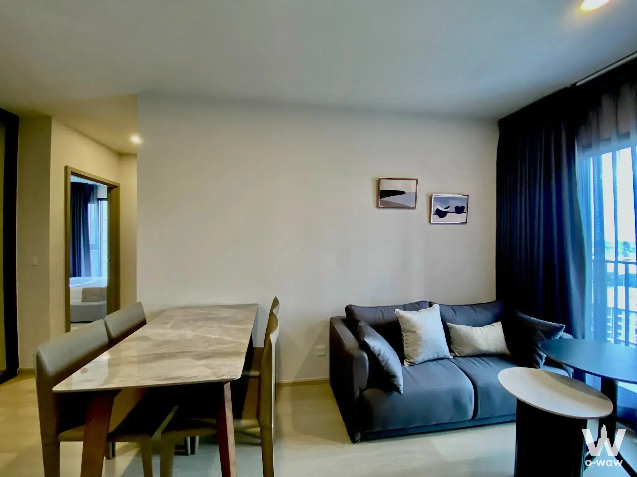 Open-plan living space in Aspire Onnut Station 2-bed condo with grey sofa, marble-top dining table, and blue curtains