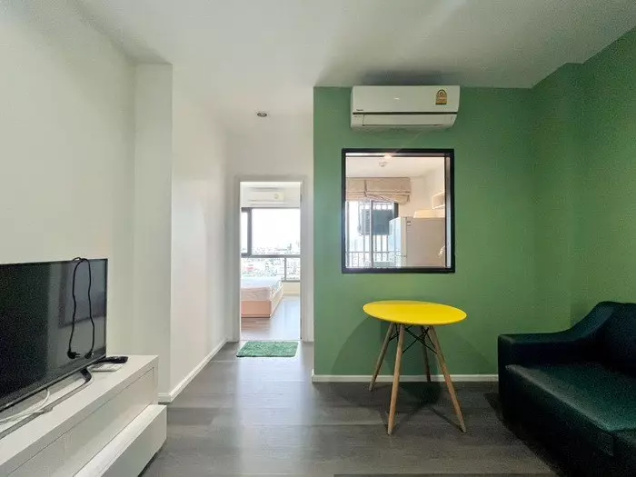 Modern living room with teal sofa and green accent wall in 1-bed rental at The Stage Taopoon Interchange Bangkok