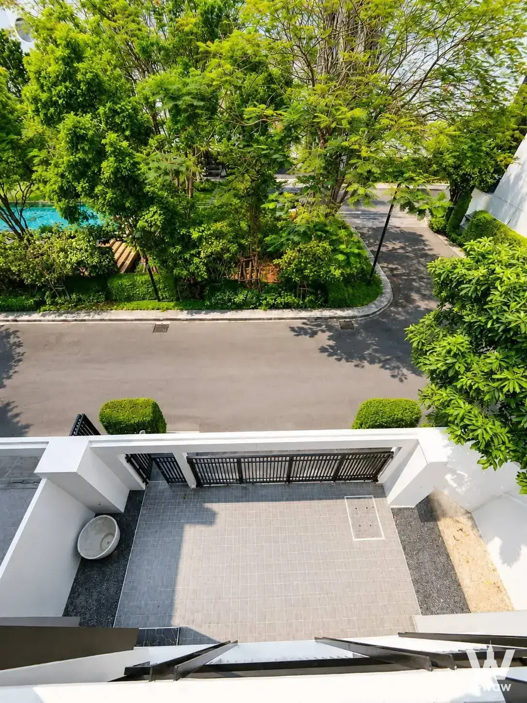 Courtyard view of 4-bed condo for sale in Noble Curve with manicured bushes, black gate, and lush green landscaping