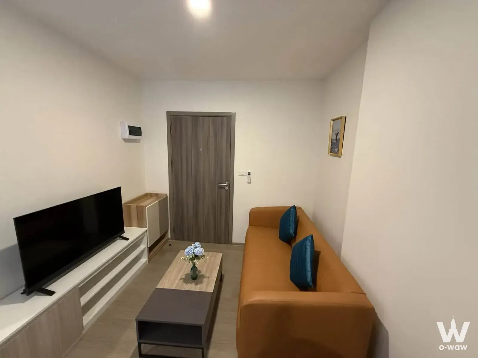 Living room in The Origin Bangkae condo with tan leather sofa, TV console, and wood flooring