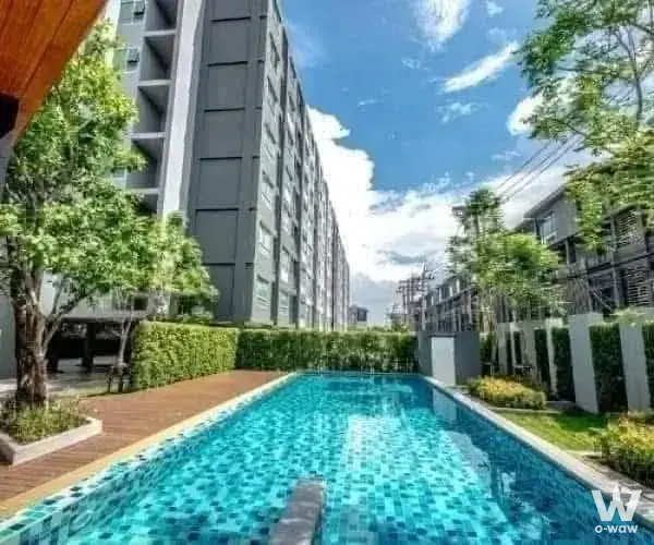 A 1-bed condo for sale in Aspire Ladprao 113 has a long turquoise pool with brick deck and high-rise backdrop