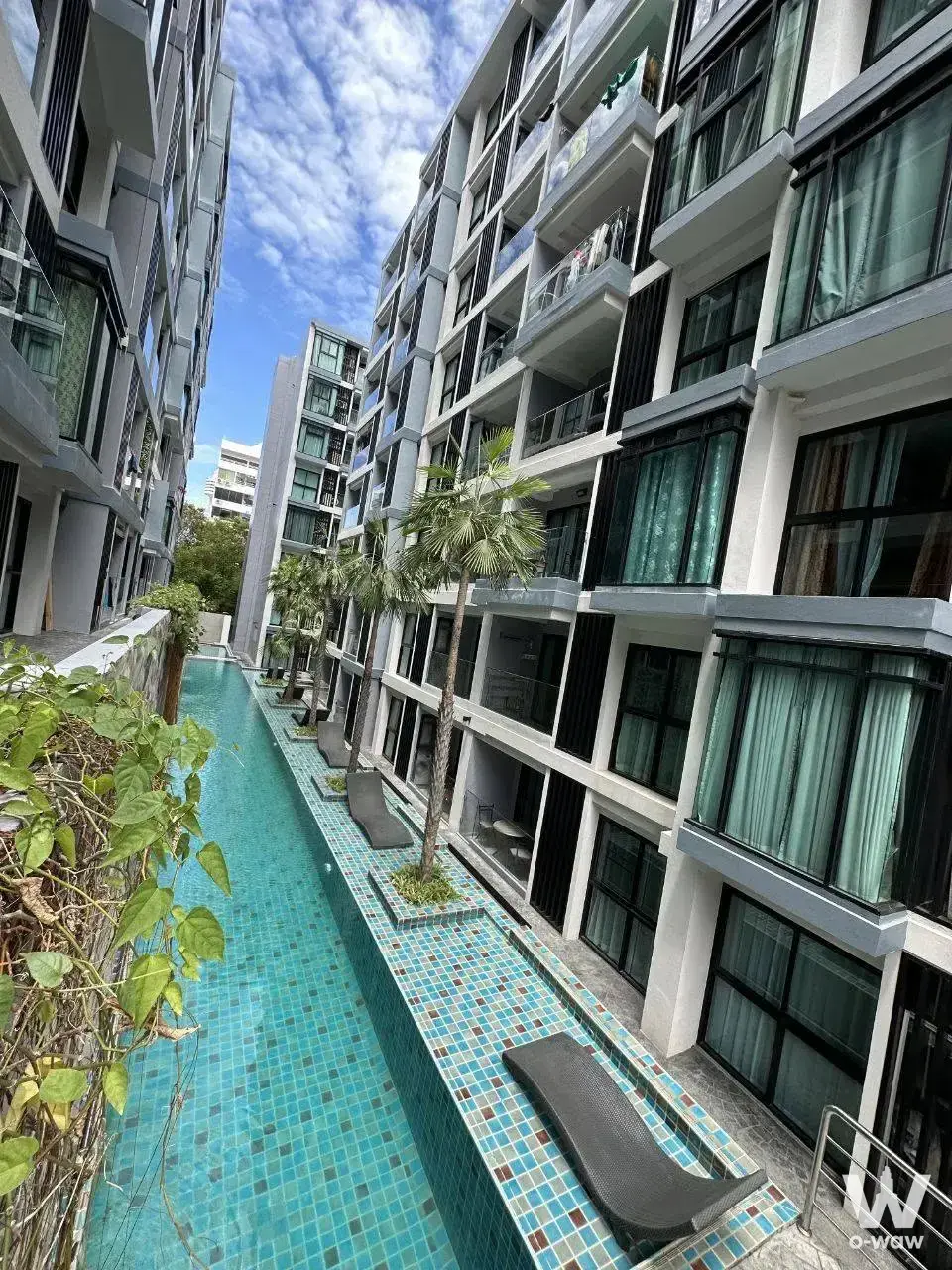 Modern condo exterior with turquoise mosaic pool, lounge chairs and palm trees in Siam Oriental Tropical Garden