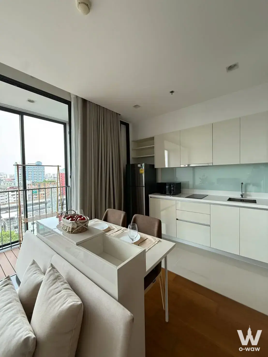 1-bed condo for rent in Bright Wongwian Yai featuring open-plan kitchen island, dining chairs, and balcony city view