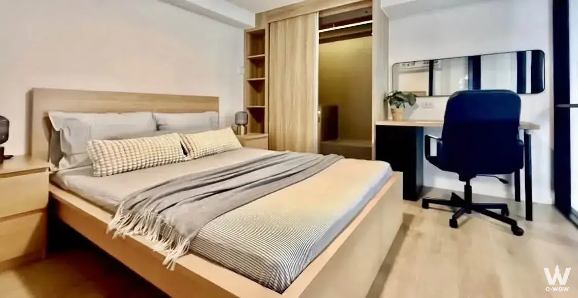 Modern bedroom in a 1-bed condo for rent in Siamese Sukhumvit 87, with a light wood bed and warm closet lighting